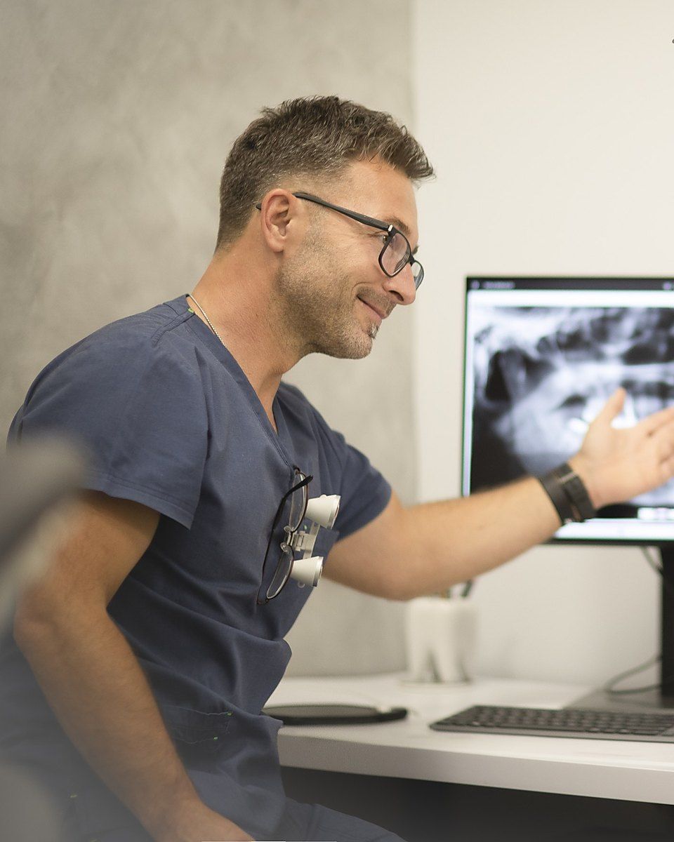 Lekarz w lupach pokazuje na monitorze pantomogram, siedząc przy biurku w gabinecie